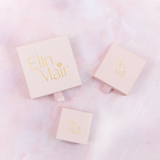 Three beige boxes with 'Elin Mair' branding on a pink background