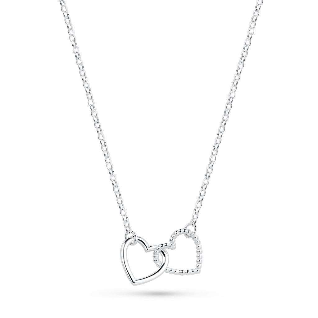 A silver Cariad necklace by Elin Mair featuring two interlocking open heart pendants, one with a smooth polished finish and the other with a textured beaded edge, suspended from a delicate cable chain against a white background.