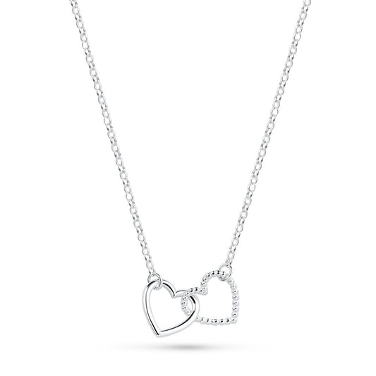 A silver Cariad necklace by Elin Mair featuring two interlocking open heart pendants, one with a smooth polished finish and the other with a textured beaded edge, suspended from a delicate cable chain against a white background.